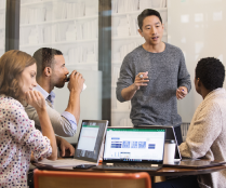 Small Business Team Collaborating In Conference Room With Three Laptops Open On Table, Graphic